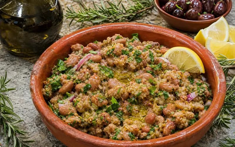 Ful médamès dans un bol en terre cuite, fèves brunes mijotées avec huile d'olive, quartiers de citron, oignon haché et persil frais, pain pita en arrière-plan